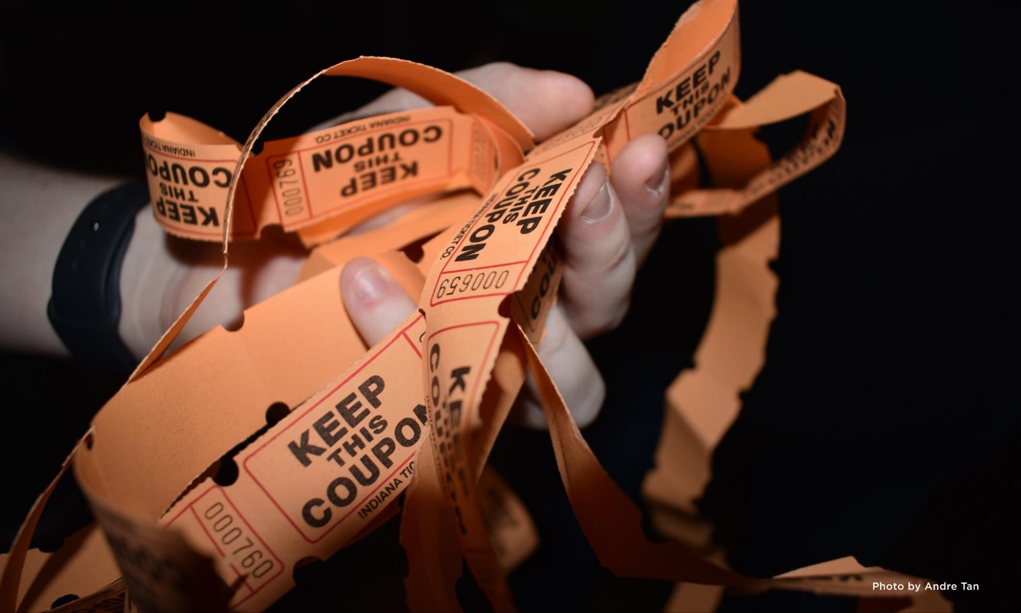 Close-up of a hand holding lots of orange coupon tickets.