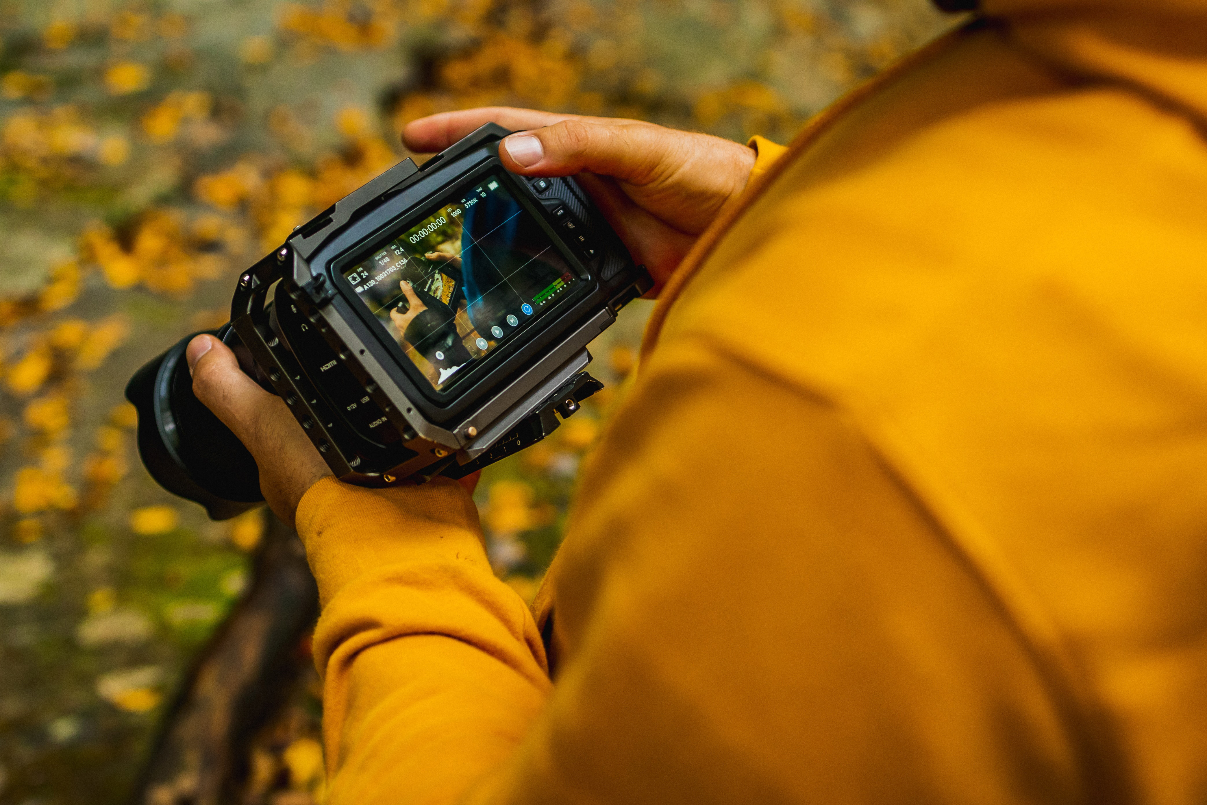 Person in a yellow jacket reviewing a digital photo on an LCD screen on the back of a camera.