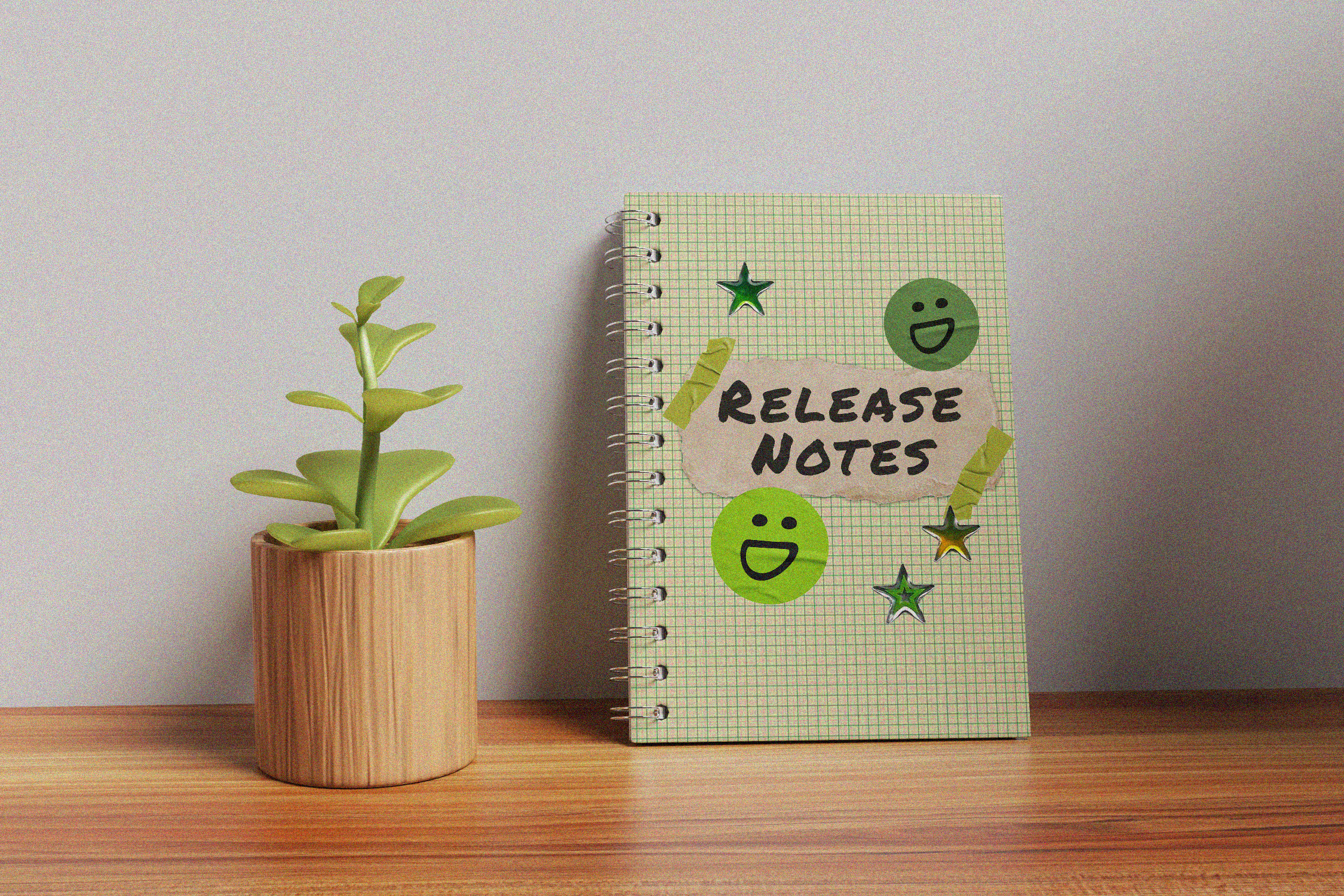 A small bamboo planter with a plant on a desk next to a notebook covered in stickers that reads, "Release Notes."