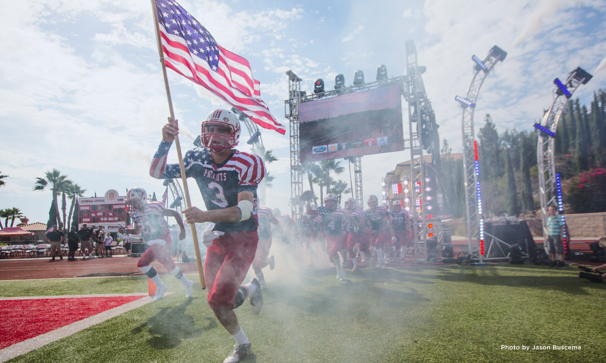 Football player carrying an American flag across a football field through a plume of smoke.